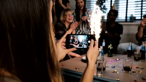 Girl-taking-a-smartphone-photo-of-birthday-party-with-sparkling-firework-and-multiethnic-friends-clapping-slow-motion