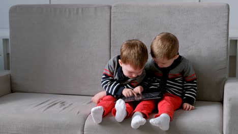 Dos-hermanos-gemelos-llevar-del-otro-tablet-sentado-en-el-sofá.-Los-niños-jugar-en-la-tablet.