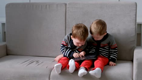 Zwei-Zwillingsbrüder-wegnehmen-des-anderen-Tablet-auf-dem-Sofa-sitzen.-Kinder-spielen-auf-dem-Tablet.