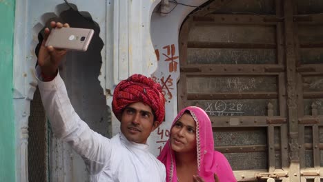 Dolly-in-to-Couple-taking-camera-selfie-on-mobile-phone-photography-in-front-of-their-house-with-traditional-architecture