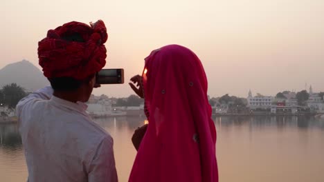 Pan-left-to-couple-in-Indian-dress-taking-photos-of-sunset-at-a-holy-lake-in-Rajasthan