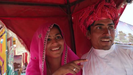 Handheld-shot-of-Indian-couple-enjoying-a-camel-ride-in-a-caravan-at-Pushkar-Fair,-Rajasthan,--India