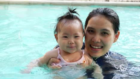 Asian-young-mother-and-adorable-curly-little-baby-girl-having-fun-in-a-swimming-pool.