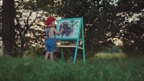 Little-boy-standing-and-drawing-on-the-easel-at-park