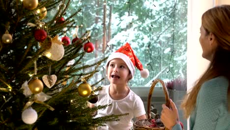 Kleine-süße-Mädchen-mit-ihrer-Mutter-schmücken-den-Weihnachtsbaum