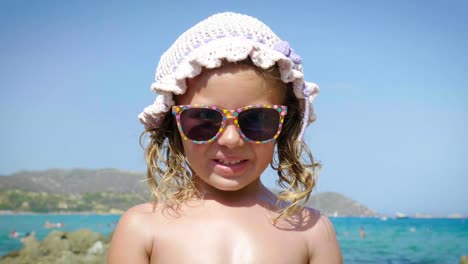 Portrait-of-beautiful-little-girl-having-fun-on-the-sea,-cute-smiling-in-panama,-sun-protection-cream,-background-of-sea-blue-water-and-rocks.