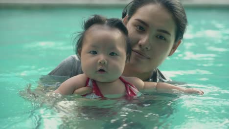 Asian-young-mother-and-adorable-curly-little-baby-girl-having-fun-in-a-swimming-pool.