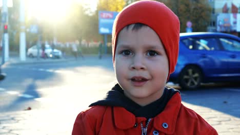 Portrait-of-a-small,-beautiful,-cheerful-boy-on-the-background-of-a-blurred-city