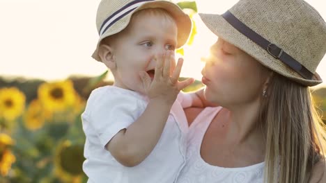 Attractive-woman-holding-a-small-child-in-her-arms-in-a-field-with-yellow-sunflowers.