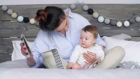 Madre-y-bebé-niña-viendo-un-libro-del-cuadro-en-la-cama