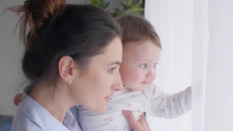 Madre-y-bebé-niña-mirando-por-la-ventana-de-interés