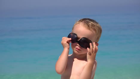 Lustige-junge-versuchen,-Sonnenbrille,-verärgert-zu-scheitern,-wunderschönen-türkisfarbenen-Meer-zu-arrangieren