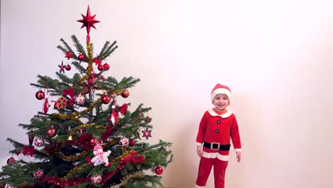 Happy-child-dressed-in-Santa-Claus-jumping-near-Christmas-tree,-waiting-presents