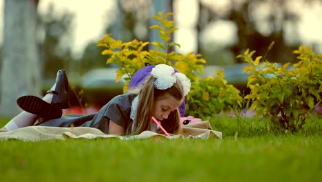 Young-girl-outdoors-lying-on-the-grass-and-drawing