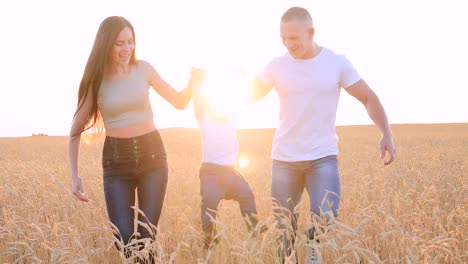 Happy-parents-hold-the-little-son-by-the-hand-and-raise-her-high,-playing-with-him.-Happy-family-in-a-wheat-field