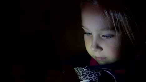 Little-girl-playing-tablet,-phone-at-night,-close-up