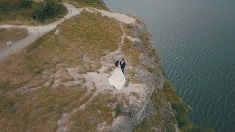 Joven-y-hermosa-pareja-junto-en-la-ladera-de-la-montaña-cerca-del-mar.-Hermoso-novio-y-novia.-Disparos-desde-el-aire.-Toma-aérea