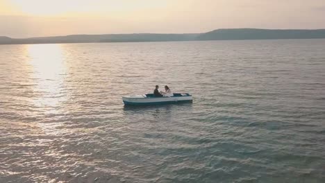 Young-and-beautiful-wedding-couple-together-sailing-on-a-boat-with-oars-on-the-sea.-Sunset.-Lovely-groom-and-bride.-Shooting-from-the-air.-Aerial-shot