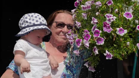 Baby-girl-with-grandmother-watering-flowers.