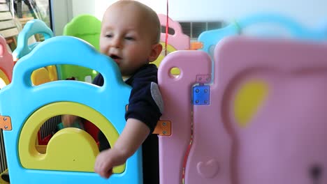 Baby-Junge-Stand-In-bunten-Laufstall