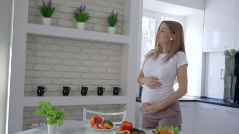 vitamin-food-for-pregnancy,-lovely-future-mother-with-big-tummy-dancing-at-kitchen-at-brunch-time-with-fresh-vegetables-and-fruits-in-apartment