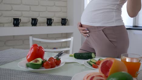 Schwangerschaft-Frau-mit-großen-Bauch-ist-nützlichen-leckeren-Salat-aus-frischem-Gemüse-für-gesundes-Essen-in-der-Küche-kochen