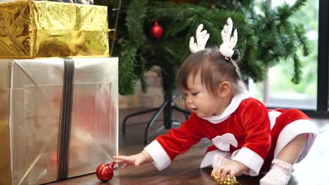 Cute-1-year-old-baby-girl-wearing-reindeer-headband-playing-with-Christmas-ornament-with-christmas-tree-in-background.-Merry-Christmas-and-Happy-Holidays!