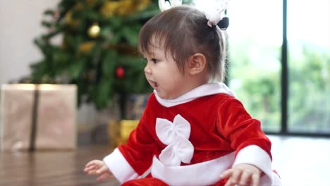 Cute-1-year-old-baby-girl-wearing-reindeer-headband-playing-with-Christmas-ornament-with-christmas-tree-in-background.-Merry-Christmas-and-Happy-Holidays!