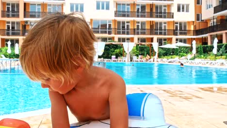 Happy-little-boy-sitting-near-the-pool