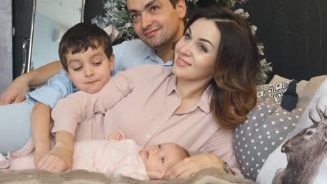 Young-family-with-son-and-newborn-lie-on-a-bed-in-Christmas