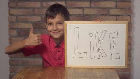 child-sitting-at-the-desk-holding-flipchart-with-lettering-like-on-the-background-red-brick-wall