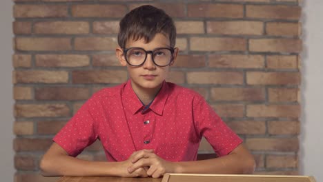 child-sitting-at-the-desk-holding-flipchart-with-lettering-it-on-the-background-red-brick-wall