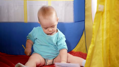 Bebé-atractivo-jugar-en-tienda-colorido-de-los-niños-en-la-casa.-El-niño-dibuja-cuidadosamente-en-cuaderno-lápiz