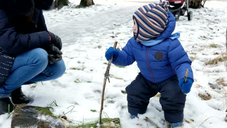 Attraktive-Baby-spielt-mit-Mutter-im-Winter-auf-der-Straße.-Der-junge-in-den-Händen-von-den-Ästen-der-Bäume