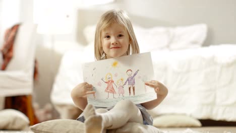 Cute-Young-Girl-Sitting-on-Pillows-Shows-Drawing-of-Her-Family.