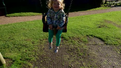 Young-toddler-girl-having-fun-in-the-British-summertime-at-the-park-on-the-swing