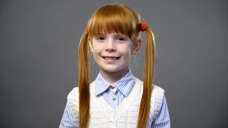 Beautiful-redhead-girl-with-two-pigtails-looking-onto-the-camera-and-smiling-against-gray-background