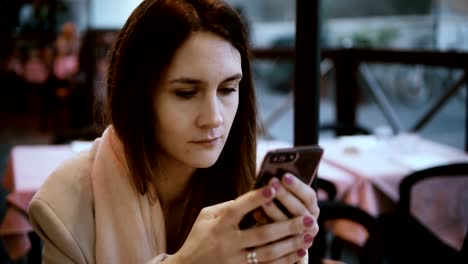 Junge-Brünette-Frau-sitzt-im-Café-und-Bestellung-warten.-Hübsche-Frau-nutzt-das-Smartphone-im-Internet-surfen