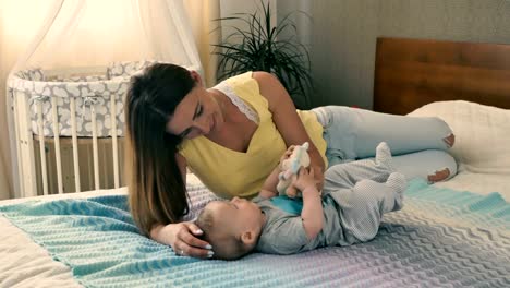 Schöne-Mutter-spielt-Stofftier-mit-ihrem-Baby-am-Bett