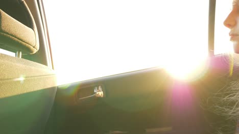 Little-girl,-bored-in-the-car.-Sun-flare.-Sunset-light-at-cars-window.-Strong-wind-fluttering-hairs.