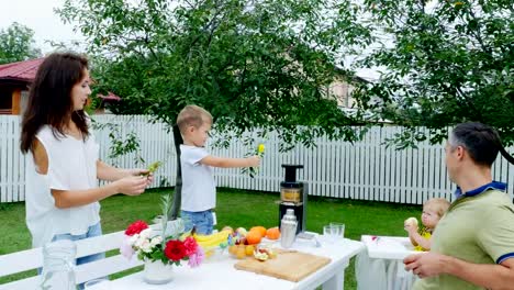 Sommer-in-den-Garten,-vier-jährigen-Jungen-hat-das-Stroh-für-Saft-eingerichtet,-bietet-ihnen-vor-seinem-Vater,-Mutter-und-jüngeren-Schwester.-Der-junge-hat-Spaß,-zeigt-seine-Zunge