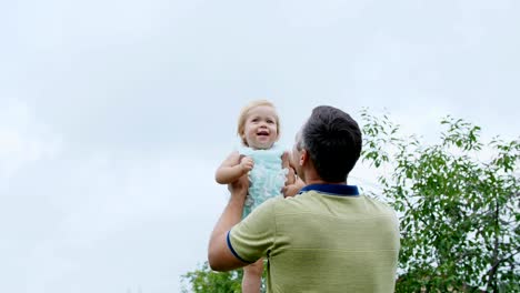 Sommer-in-den-Garten,-Mutter,-eine-Ansicht-von-unten,-der-Papa-wirft-seine-ein-jährige-Tochter,-spielt-mit-ihr,-hat-Spaß.-Sie-lacht.-die-Familie-verbringt-ihre-Freizeit-zusammen