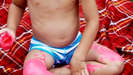 a-little-child,-a-four-year-old-boy-playing,-painting-with-finger-paints,-decorating-himself,-in-the-garden,-sitting-on-a-blanket,-on-grass,-lawn,-in-the-summer.-he's-having-fun