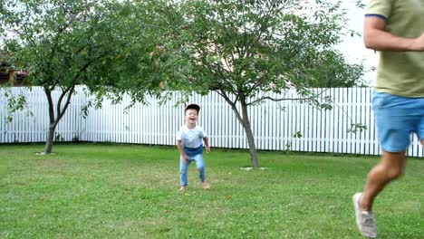 Papá-con-un-hijo-de-cuatro-años-jugando-a-la-pelota,-fútbol,-en-el-patio-en-un-césped-verde,-en-el-verano