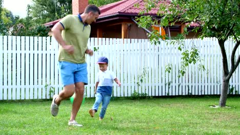 Papá-con-un-hijo-de-cuatro-años-jugando-a-la-pelota,-fútbol,-en-el-patio-en-un-césped-verde,-en-el-verano