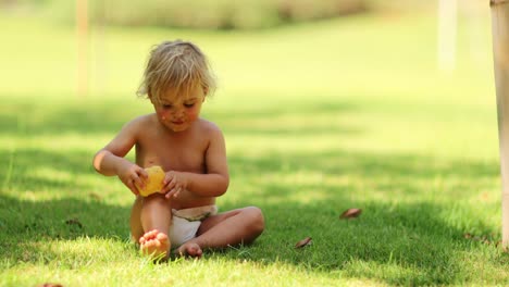 Adorable-candid-cute-moment-of-infant-toddler-boy-playing-with-pear-fruit-while-sitting-in-the-grass-outdoors-in-the-sunlight-in-4k-clip-resolution