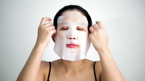 Young-woman-doing-facial-mask-sheet-with-purifying-mask-on-her-face-on-white-background