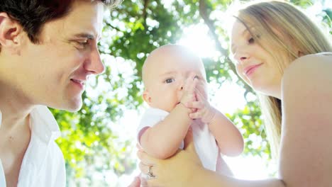 Portrait-of-European-parents-outdoors-kissing-baby-boy