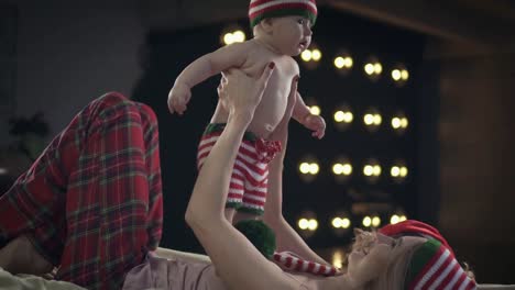 Madre-hermosa-en-ropa-de-Navidad-es-acostado-en-cama-y-jugar-con-su-hijo-de-bebé-sonriente