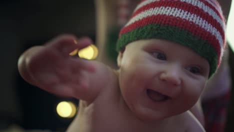 Happy-baby-boy-in-striped-pants-and-cap-is-sitting-on-bed,-looking-in-camera,-smiling-and-playing.-Portrait